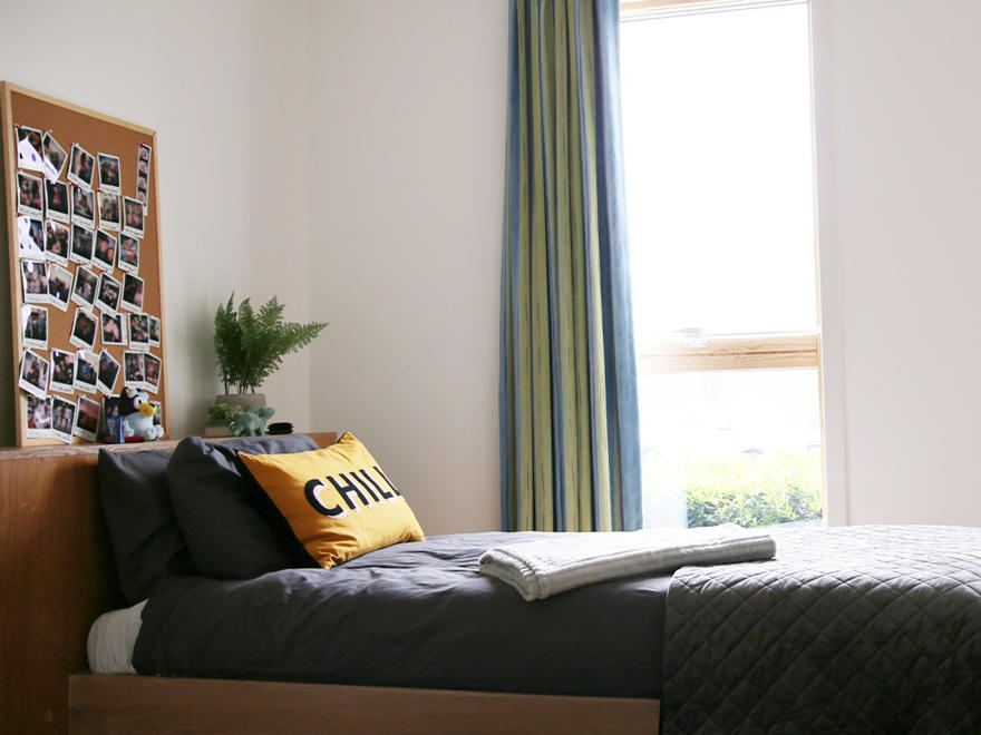 A bed in a student's room with photos pinned to a noticeboard